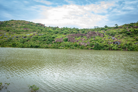 View of Lamingo Dam surrounded by rocky hills and lush vegetation under a cloudy sky in Jos Plateau Nigeria.