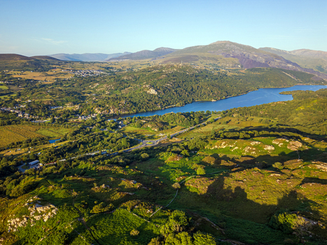 Aerial view of Cwm y glo village nestled in the lush green landscape of Snowdonia featuring a serene lake winding roads and rolling hills in Cwm y glo Wales United Kingdom. Aerial view of Cwm y glo village nestled in the lush green landscape of Snowdonia featuring a serene lake winding roads and rolling hills in Cwm y glo Wales United Kingdom.