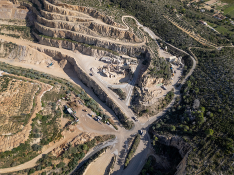 Aerial view of a large open pit stone quarry with terraced rock faces heavy machinery and access roads in Teulada Valencian Community Spain.