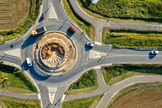 Aerial view of Kersbacher Kreisel roundabout with cars and a yellow truck navigating the circular road surrounded by green fields and construction in Forchheim Bavaria Germany.