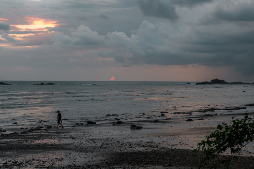 View of a person walking along a rocky beach at dusk with dark clouds over the ocean in Costa Rica.