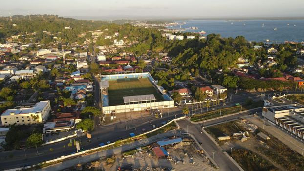 Aerial view of a soccer stadium surrounded by urban buildings lush green hills and the coastal bay in Sorong Southwest Papua Indonesia. Aerial view of a soccer stadium surrounded by urban buildings lush green hills and the coastal bay in Sorong Southwest Papua Indonesia.