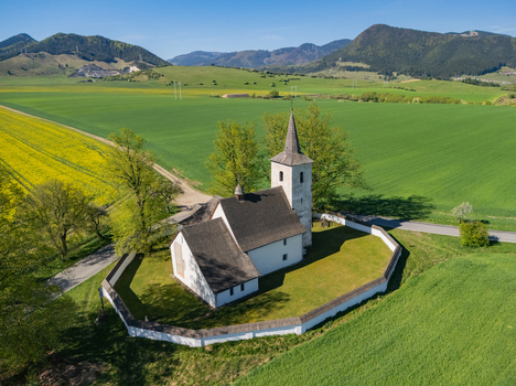 Aerial view of the historic Church of All Saints surrounded by a stone wall and vibrant green fields in Ludrova Zilina Region Slovakia. Aerial view of the historic Church of All Saints surrounded by a stone wall and vibrant green fields in Ludrova Zilina Region Slovakia.