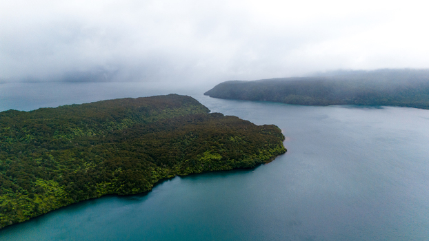 Aerial view of dark waters embrace land masses cloaked in deep green foliage under a blanket of heavy mist Manapouri New Zealand. Aerial view of dark waters embrace land masses cloaked in deep green foliage under a blanket of heavy mist Manapouri New Zealand.