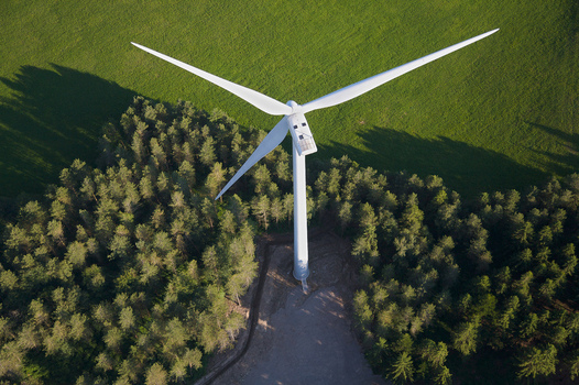 Aerial view of a towering wind turbine stands amidst a dense forest and a field of green contrasting sharply with the natural landscape Salles Curan Occitanie France. Aerial view of a towering wind turbine stands amidst a dense forest and a field of green contrasting sharply with the natural landscape Salles Curan Occitanie France.