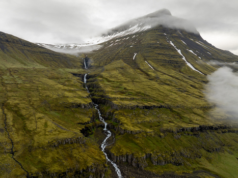 Aerial view of a cascading waterfall flowing down the mossy green slopes of a mountain in the Eastern Region of Iceland. Aerial view of a cascading waterfall flowing down the mossy green slopes of a mountain in the Eastern Region of Iceland.
