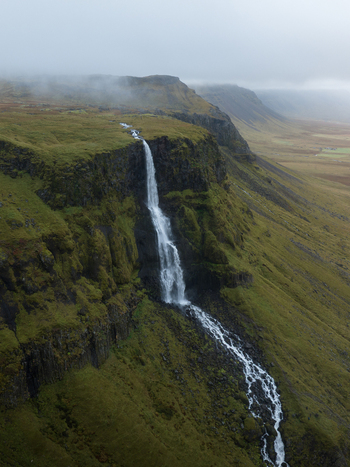 Aerial view of a striking waterfall cascading down a moss covered cliff face into a stream Snæfellsnes Iceland. Aerial view of a striking waterfall cascading down a moss covered cliff face into a stream Snæfellsnes Iceland.