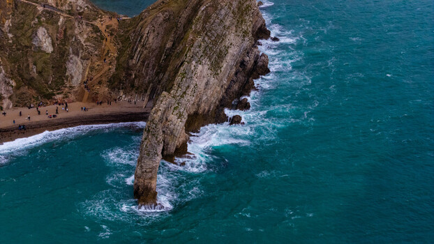 Aerial view of Durdle Door showing the limestone arch turquoise sea waves and a pebble beach with people walking along the coast in Wareham England United Kingdom. Aerial view of Durdle Door showing the limestone arch turquoise sea waves and a pebble beach with people walking along the coast in Wareham England United Kingdom.