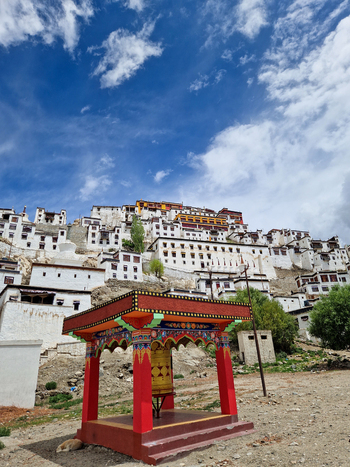 View of the historic Thiksey Monastery with its tiered white buildings and a vibrant prayer wheel in the foreground under a blue sky in Thiksey Ladakh India.