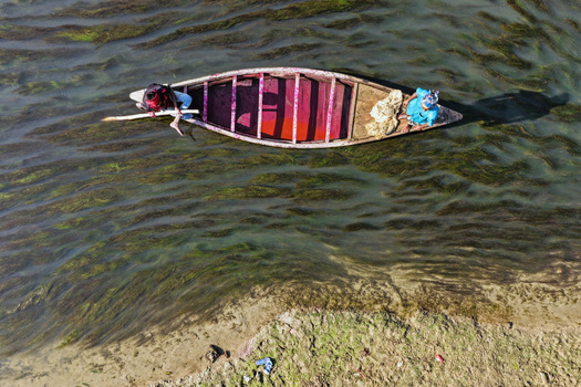 Aerial view of a small wooden boat with two fishermen navigating a river filled with aquatic vegetation in Joypurhat Rajshahi Division Bangladesh. Aerial view of a small wooden boat with two fishermen navigating a river filled with aquatic vegetation in Joypurhat Rajshahi Division Bangladesh.