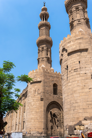 View of the historic Bab Zuwayla gate and its ornate stone minaret with intricate carvings under a clear blue sky in El Darb El Ahmar Cairo Egypt. View of the historic Bab Zuwayla gate and its ornate stone minaret with intricate carvings under a clear blue sky in El Darb El Ahmar Cairo Egypt.