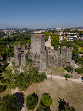 Aerial view of Guimaraes Castle with its stone walls and towers surrounded by lush green trees and the historic cityscape of Guimaraes Braga Portugal. Aerial view of Guimaraes Castle with its stone walls and towers surrounded by lush green trees and the historic cityscape of Guimaraes Braga Portugal.