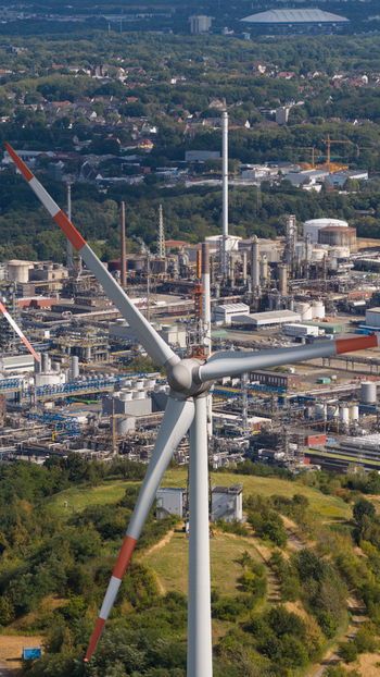 Aerial view of a wind turbine standing in front of the Tanklager industrial complex with storage tanks pipelines and factory buildings in Gelsenkirchen North Rhine Westphalia Germany.