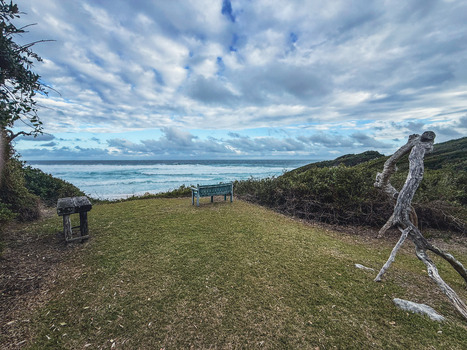 View of a wooden bench and driftwood sculpture on a grassy cliff overlooking the ocean waves under a cloudy sky in Plettenberg Bay Western Cape South Africa. View of a wooden bench and driftwood sculpture on a grassy cliff overlooking the ocean waves under a cloudy sky in Plettenberg Bay Western Cape South Africa.