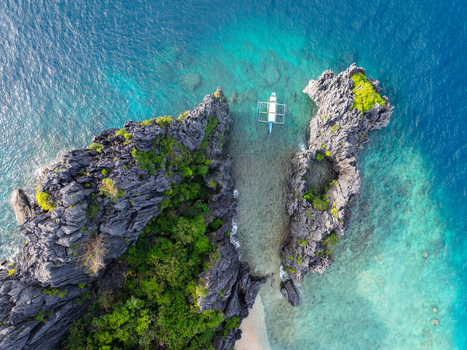 Aerial view of a traditional bangka boat anchored in a turquoise cove by the limestone cliffs of Shimizu Island in El Nido MIMAROPA Philippines.