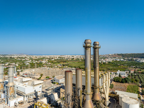 Aerial view of a power plant with tall industrial chimneys and an electrical substation surrounded by green fields and the city of Chania in the distance Chania Greece.