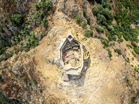 Aerial view of Castello del Volterraio a historic stone fortress perched on a rocky hilltop surrounded by dry Mediterranean vegetation and rugged terrain in Portoferraio Toscana Italy.