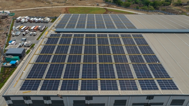 Aerial view of a large warehouse roof covered with an extensive array of solar panels featuring industrial trucks parked in the adjacent lot in Bhiwandi Maharashtra India. Aerial view of a large warehouse roof covered with an extensive array of solar panels featuring industrial trucks parked in the adjacent lot in Bhiwandi Maharashtra India.