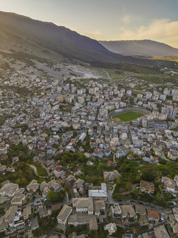 Aerial view of the historic city of Gjirokaster with its traditional stone houses and stadium nestled in the mountains of Gjirokaster Gjirokaster County Albania. Aerial view of the historic city of Gjirokaster with its traditional stone houses and stadium nestled in the mountains of Gjirokaster Gjirokaster County Albania.