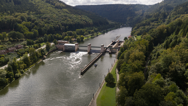 Aerial view of the Neckar Staustufe und Schleuse Rockenau lock on the Neckar river surrounded by dense green forests and rolling hills in Eberbach Baden Wurttemberg Germany.