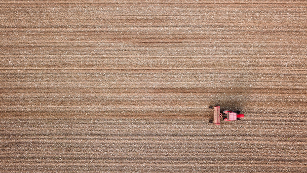 Aerial view of a red tractor ploughing a large brown agricultural field with visible soil furrows in Neuf Brisach Grand Est France. Aerial view of a red tractor ploughing a large brown agricultural field with visible soil furrows in Neuf Brisach Grand Est France.