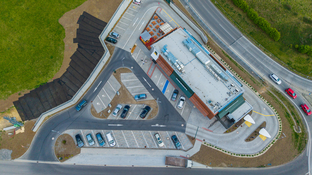 Aerial view of a modern McDonald s fast food restaurant with a drive thru lane parking lot with cars and people walking near the entrance next to a green field. Aerial view of a modern McDonald s fast food restaurant with a drive thru lane parking lot with cars and people walking near the entrance next to a green field.