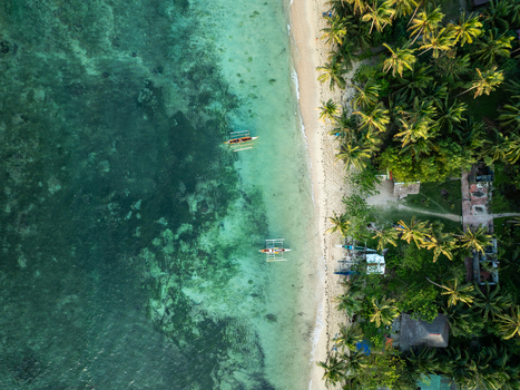 Aerial view of Mahaybo Beach featuring turquoise waters traditional outrigger boats and lush palm trees along the sandy coastline in General Luna Caraga Philippines. Aerial view of Mahaybo Beach featuring turquoise waters traditional outrigger boats and lush palm trees along the sandy coastline in General Luna Caraga Philippines.