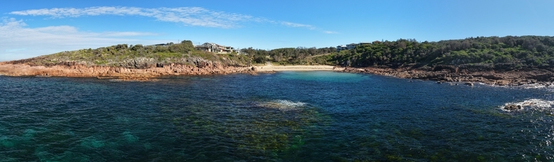 Aerial view of where the serene beach meets rugged red sandstone cliffs showcasing the turquoise waters contrasting with the deep blue sea Bate Bay New South Wales Australia. Aerial view of where the serene beach meets rugged red sandstone cliffs showcasing the turquoise waters contrasting with the deep blue sea Bate Bay New South Wales Australia.