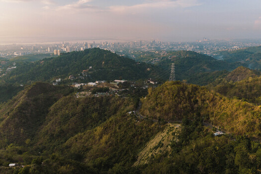 Aerial view of the lush green hills of Busay overlooking the distant urban skyline and coastal landscape of Cebu City Central Visayas Philippines.