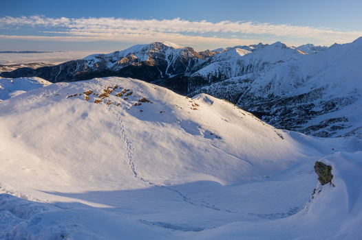 View of Ornak peak in the Western Tatras covered in deep snow with footprints leading up the slope under a clear blue sky in Tatra County Lesser Poland Voivode Poland. View of Ornak peak in the Western Tatras covered in deep snow with footprints leading up the slope under a clear blue sky in Tatra County Lesser Poland Voivode Poland.