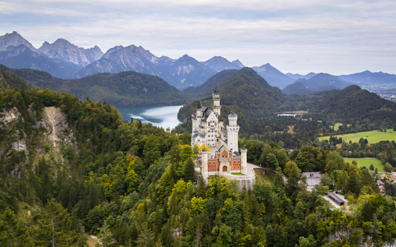 Aerial view of the majestic Neuschwanstein Castle atop a vibrant hill framed by tranquil Alpsee lake and the distant rugged Alps Neuschwanstein Castle Bayern Germany. Aerial view of the majestic Neuschwanstein Castle atop a vibrant hill framed by tranquil Alpsee lake and the distant rugged Alps Neuschwanstein Castle Bayern Germany.
