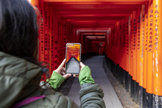 View of a woman taking a photo with her smartphone of the Senbon Torii Thousand Torii Gates at Fushimi Inari taisha shrine in Kyoto Kyoto Japan.
