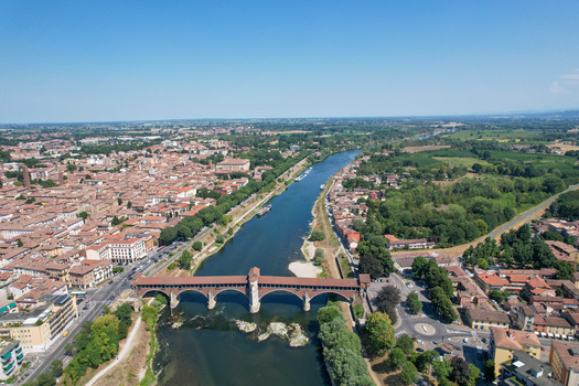 Aerial view of the historic Ponte Coperto spanning the Ticino River with the city skyline and lush greenery Pavia Lombardy Italy. Aerial view of the historic Ponte Coperto spanning the Ticino River with the city skyline and lush greenery Pavia Lombardy Italy.