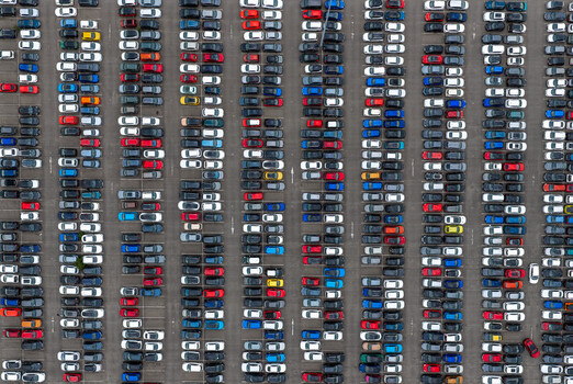 Aerial view of a large parking lot filled with numerous cars parked in organized rows in the United Kingdom. Aerial view of a large parking lot filled with numerous cars parked in organized rows in the United Kingdom.
