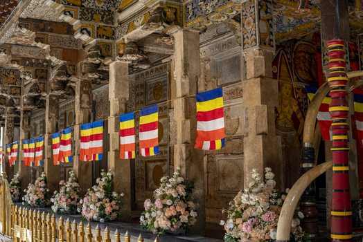 View of the ornate stone pillars and intricate carvings of the Sri Dalada Maligawa decorated with colorful Buddhist prayer flags and floral arrangements in Kandy Central Province Sri Lanka. View of the ornate stone pillars and intricate carvings of the Sri Dalada Maligawa decorated with colorful Buddhist prayer flags and floral arrangements in Kandy Central Province Sri Lanka.