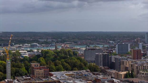 Aerial view of the port area modern buildings a construction crane and lush green trees under a cloudy sky in Southampton England United Kingdom. Aerial view of the port area modern buildings a construction crane and lush green trees under a cloudy sky in Southampton England United Kingdom.