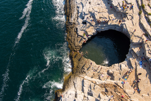 Greece 21 September 2026 Aerial view of the Giola natural pool a rock carved lagoon with turquoise water surrounded by rugged cliffs and people swimming on the sunny coastline. Greece 21 September 2026 Aerial view of the Giola natural pool a rock carved lagoon with turquoise water surrounded by rugged cliffs and people swimming on the sunny coastline.
