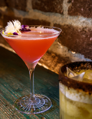 View of a pink cocktail garnished with edible flowers in a martini glass on a rustic wooden table at Ruba s Bakery Bistro in San Jose del Cabo Baja California Sur Mexico.