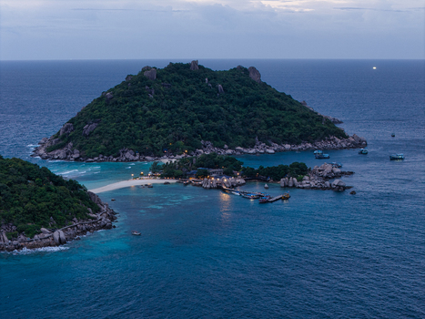 Aerial view of the lush green hills rocky coastline and turquoise waters surrounding Ko Tao island with small boats anchored near the shore in Ko Tao Surat Thani Thailand.