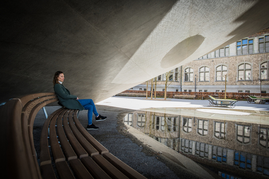 Zurich Switzerland 02 April 2023 View of a woman sitting on a curved bench under a concrete structure reflecting the National Museum in a puddle. Zurich Switzerland 02 April 2023 View of a woman sitting on a curved bench under a concrete structure reflecting the National Museum in a puddle.
