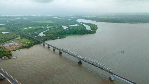 Aerial view of the Zuari Bridge spanning the Zuari River surrounded by lush mangrove forests and wetlands under a cloudy sky in Cortalim Goa India.