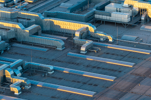 Aerial view of a large industrial rooftop featuring complex metal HVAC ductwork ventilation systems and rows of skylights illuminated by golden hour light in mazowieckie Poland. Aerial view of a large industrial rooftop featuring complex metal HVAC ductwork ventilation systems and rows of skylights illuminated by golden hour light in mazowieckie Poland.