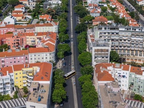 Aerial view of residential streets in Alges featuring colorful apartment buildings lush green trees lining the road and a bus driving through the neighborhood in Alges Lisbon Portugal.
