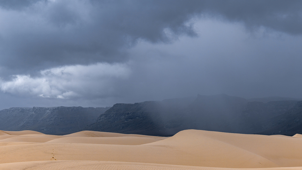 View of sand dunes under a dramatic stormy sky with dark clouds and distant mountains in Da ira Socotra Yemen.