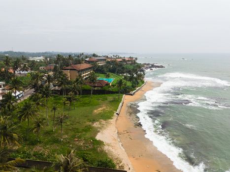 Aerial view of a coastal resort with a swimming pool and palm trees along the sandy beach and turquoise ocean waves in Galle Southern Province Sri Lanka. Aerial view of a coastal resort with a swimming pool and palm trees along the sandy beach and turquoise ocean waves in Galle Southern Province Sri Lanka.