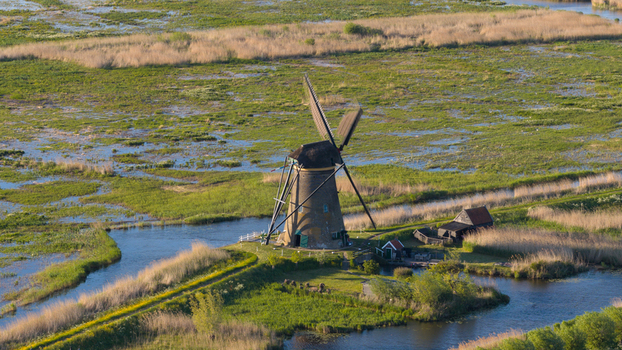 Aerial view of a historic Kinderdijk windmill surrounded by lush green marshland and narrow water canals in Kinderdijk South Holland Netherlands. Aerial view of a historic Kinderdijk windmill surrounded by lush green marshland and narrow water canals in Kinderdijk South Holland Netherlands.