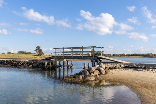 View of the wooden bridge on the island of Hjarno with a sandy shoreline and calm water under a blue sky in Hjarno Hedensted Municipality Denmark. View of the wooden bridge on the island of Hjarno with a sandy shoreline and calm water under a blue sky in Hjarno Hedensted Municipality Denmark.