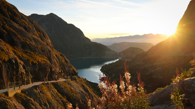 View of Lac du Vieux Emosson surrounded by rocky mountain cliffs and wildflowers during golden hour in Finhaut Valais Switzerland. View of Lac du Vieux Emosson surrounded by rocky mountain cliffs and wildflowers during golden hour in Finhaut Valais Switzerland.