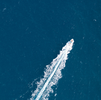 Aerial view of a small motorboat leaving a white wake in the deep blue waters of the Riserva Naturale Orientata dello Zingaro near San Vito Lo Capo Sicilia Italy. Aerial view of a small motorboat leaving a white wake in the deep blue waters of the Riserva Naturale Orientata dello Zingaro near San Vito Lo Capo Sicilia Italy.