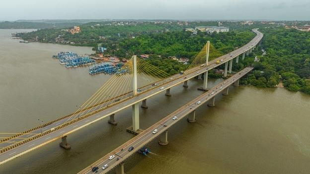 Aerial view of the Atal Setu Goa cable stayed bridge spanning the Mandovi River with traffic flowing across and fishing boats moored nearby in Panaji Goa India.